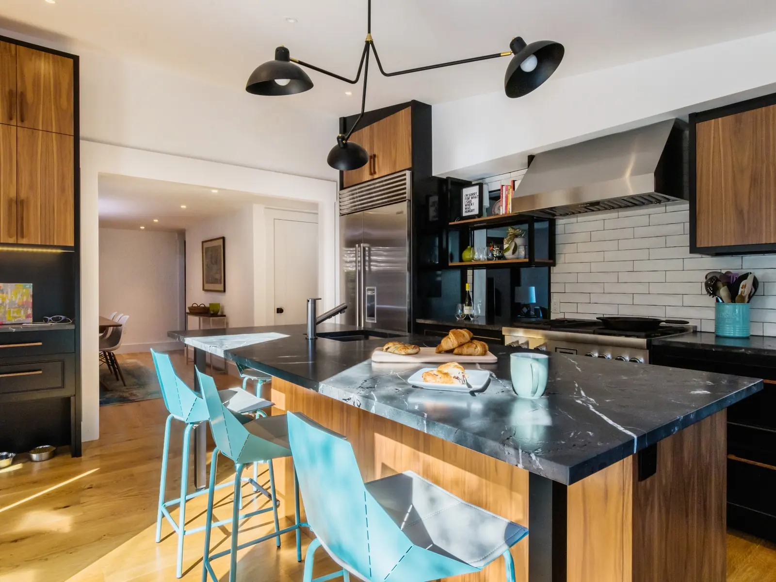 Kitchen with a black stone island, teal stools and walnut cabinetry
