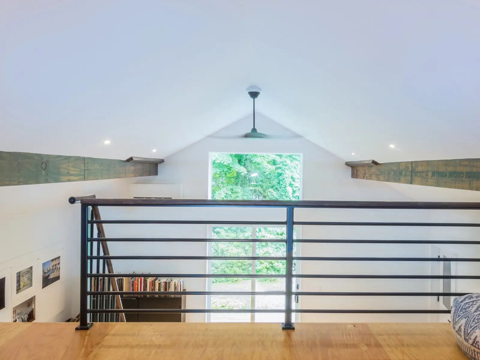 Loft landing with a black metal railing, rustic beams and a gable window