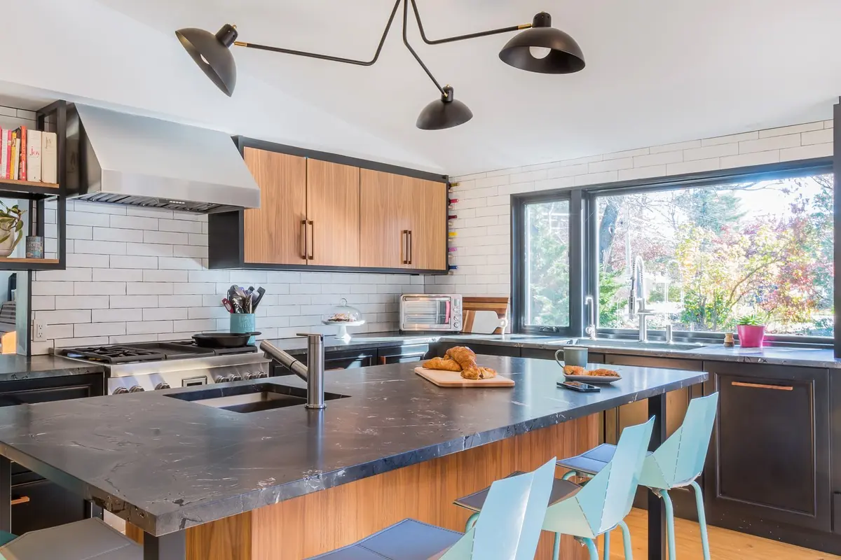 Kitchen island in dark stone and wood under a sculptural light fixture