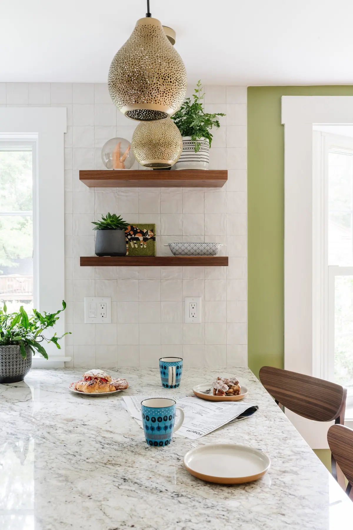 Stone counter under a pierced metal pendant and floating wood shelves