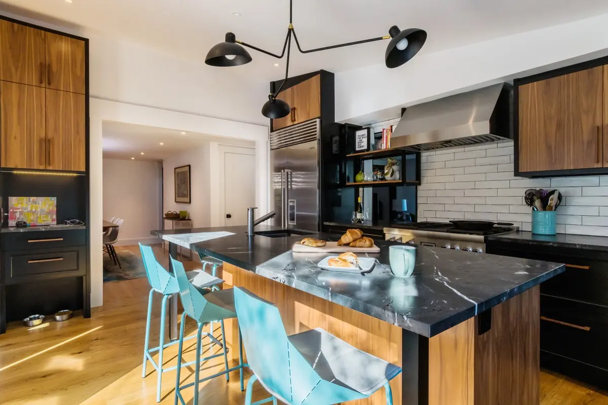 Kitchen with a black stone island, teal stools and walnut cabinetry